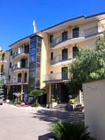 Un hotel de varios pisos con balcones, una escalera central y un estacionamiento.