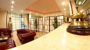 Un vestíbulo de hotel con sofás de cuero, un mostrador de recepción de mármol y un objeto decorativo de latón.