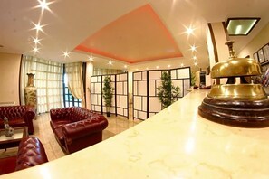Un vestíbulo de hotel con sofás de cuero, un mostrador de recepción de mármol y un objeto decorativo de latón.