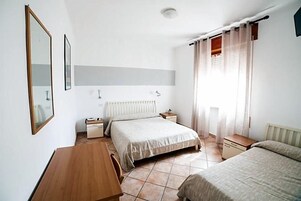 A bedroom with a bed, a desk, a chair, a radiator, and a window with curtains.