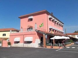 A pink building with a bar on the ground floor, a flag, and outdoor seating.