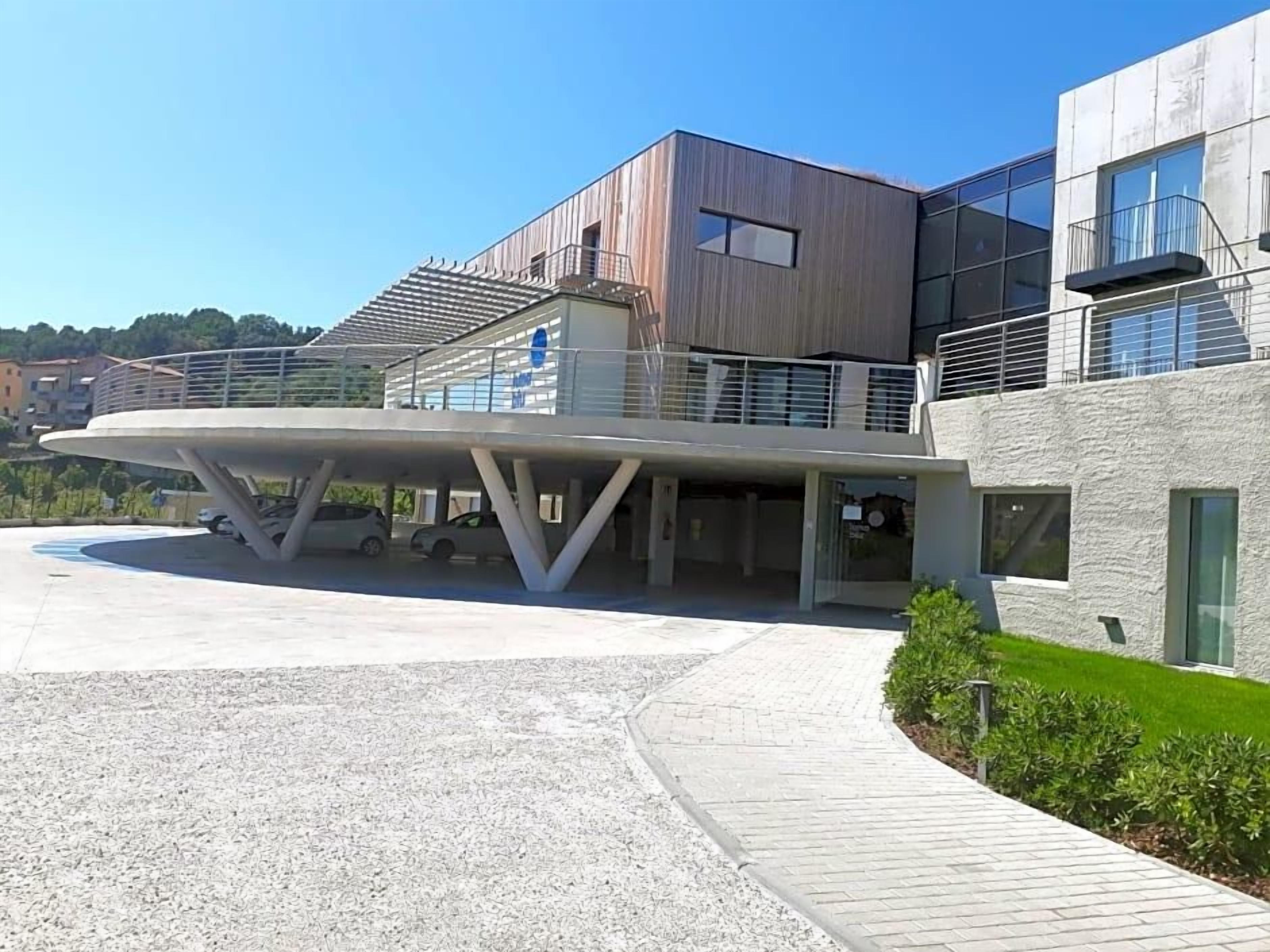 A modern building with a covered entrance, a parking area, and a landscaped garden.