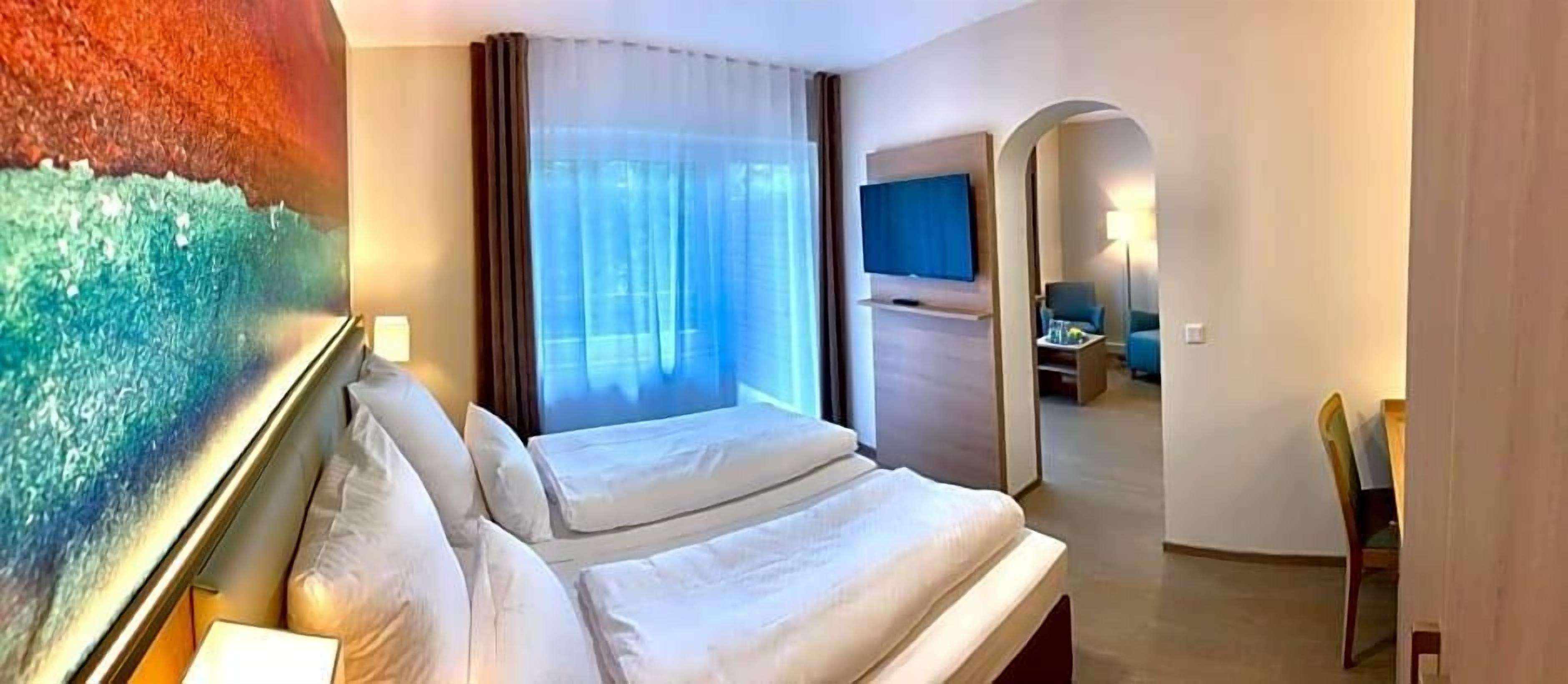 A hotel room with a bed, a television, a desk, and a view of the outdoors.