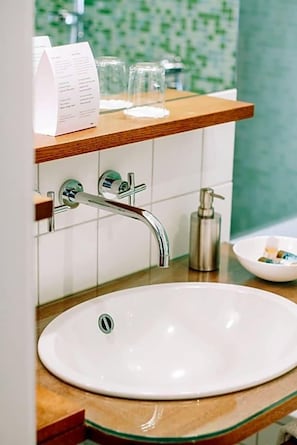 A bathroom with a white sink, a wooden countertop, a mirror, and a shelf with a menu and glasses.