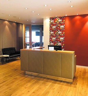A reception area with a wooden floor, a reception desk, and a red wall with a floral pattern.
