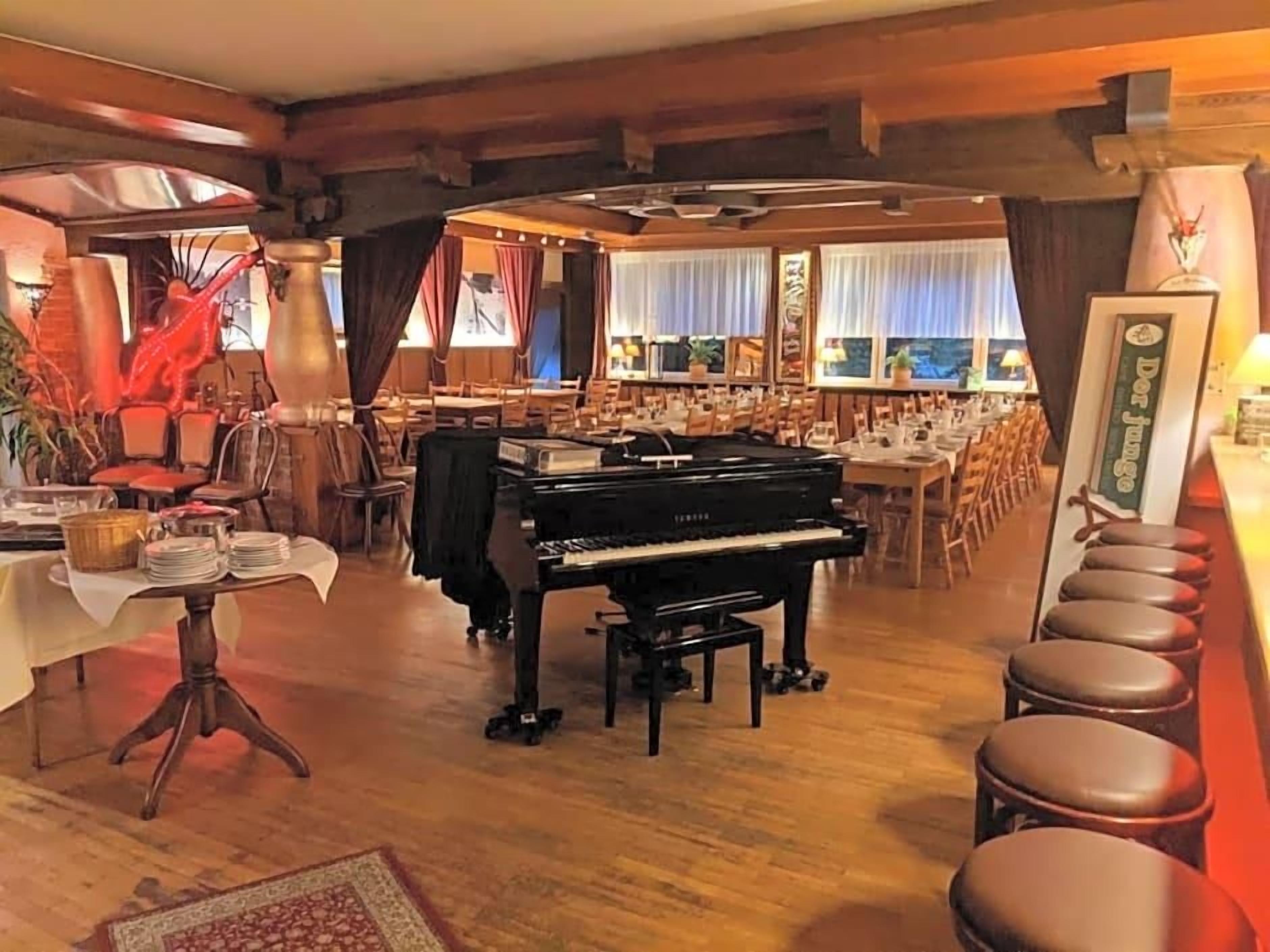 Une pièce comprenant un piano à queue, un coin repas et un bar avec des tabourets.