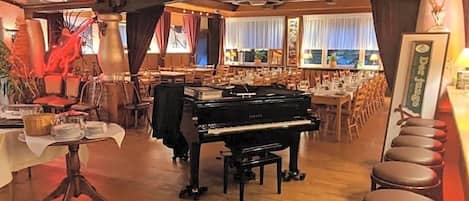 A room with a grand piano, a dining area, and a bar with stools.