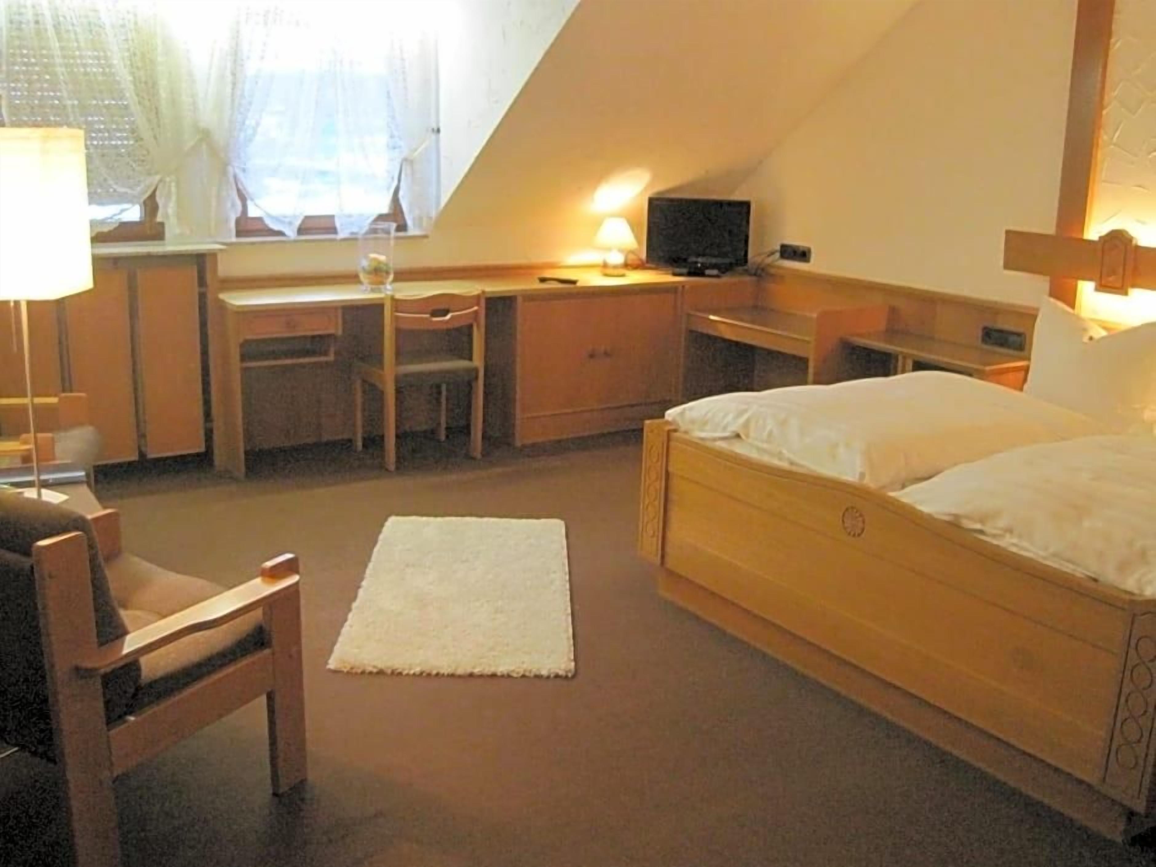 A bedroom with a bed, desk, chair, and a television.