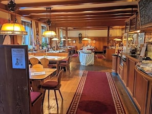Um hall de hotel com piso de madeira, várias mesas de jantar e uma mesa redonda central.