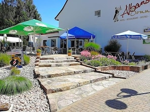 Entrada de hotel com área de estar ao ar livre, degraus de pedra e uma placa de boas-vindas.