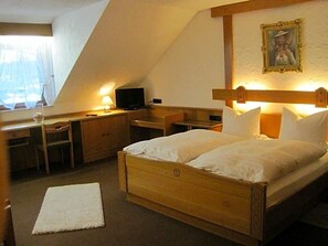 Quarto com cama, escrivaninha, cadeira e televisão.