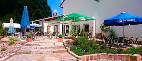 Un espacio al aire libre con mesas, sillas, sombrillas y un edificio con señalización.