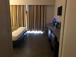 Una habitación de hotel con cama, escritorio, silla, televisor y un pequeño árbol de Navidad.