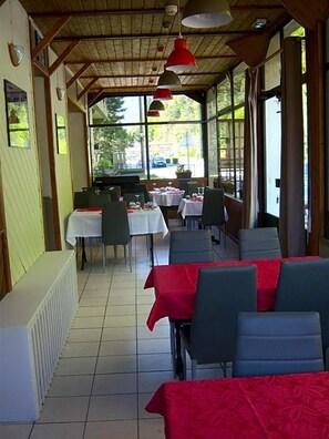 Espaço de refeições interno com mesas, cadeiras, teto de madeira e janelas amplas.