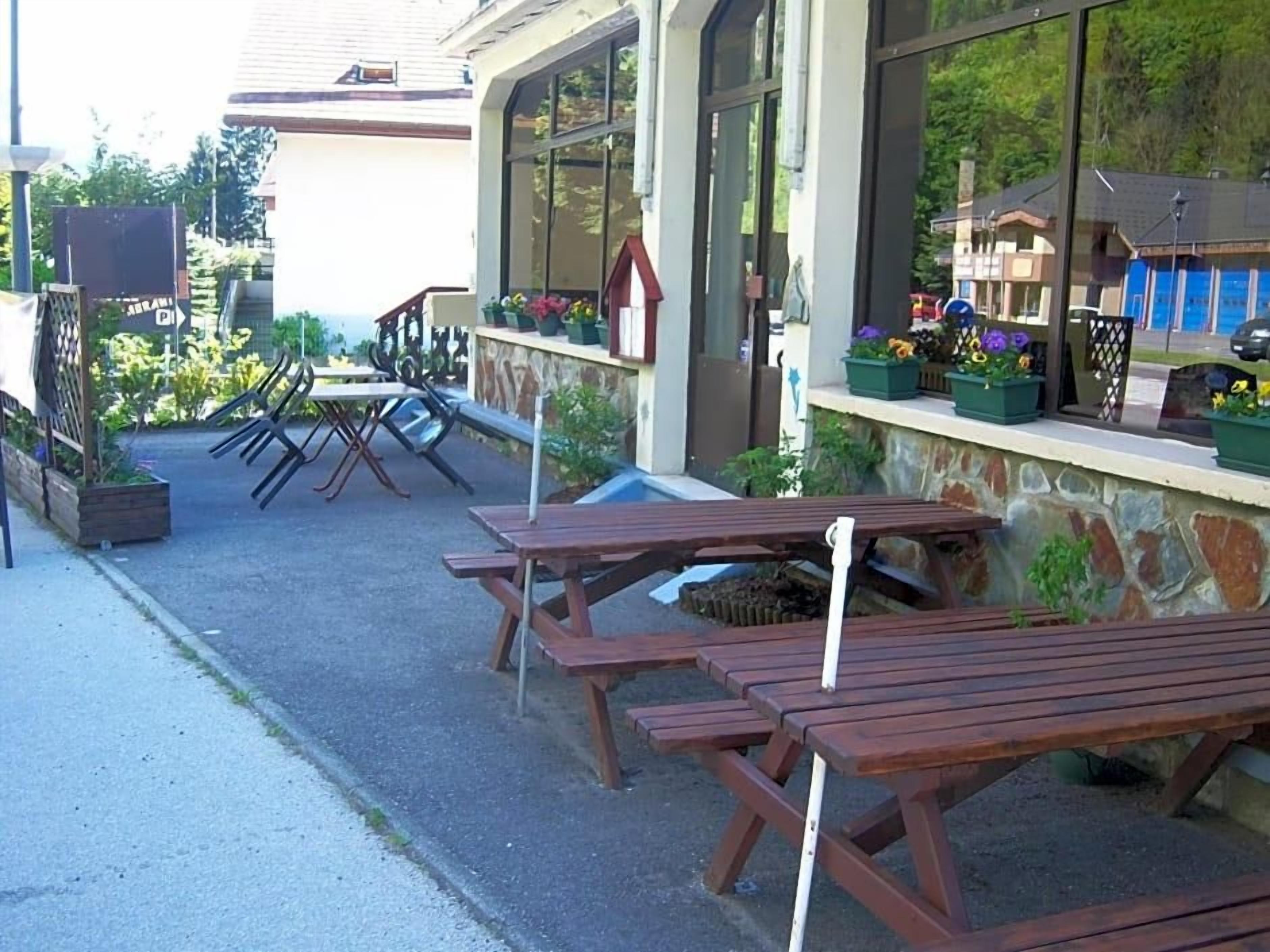Mesas y bancos de madera para picnic al aire libre, un muro de piedra y un edificio con grandes ventanales.