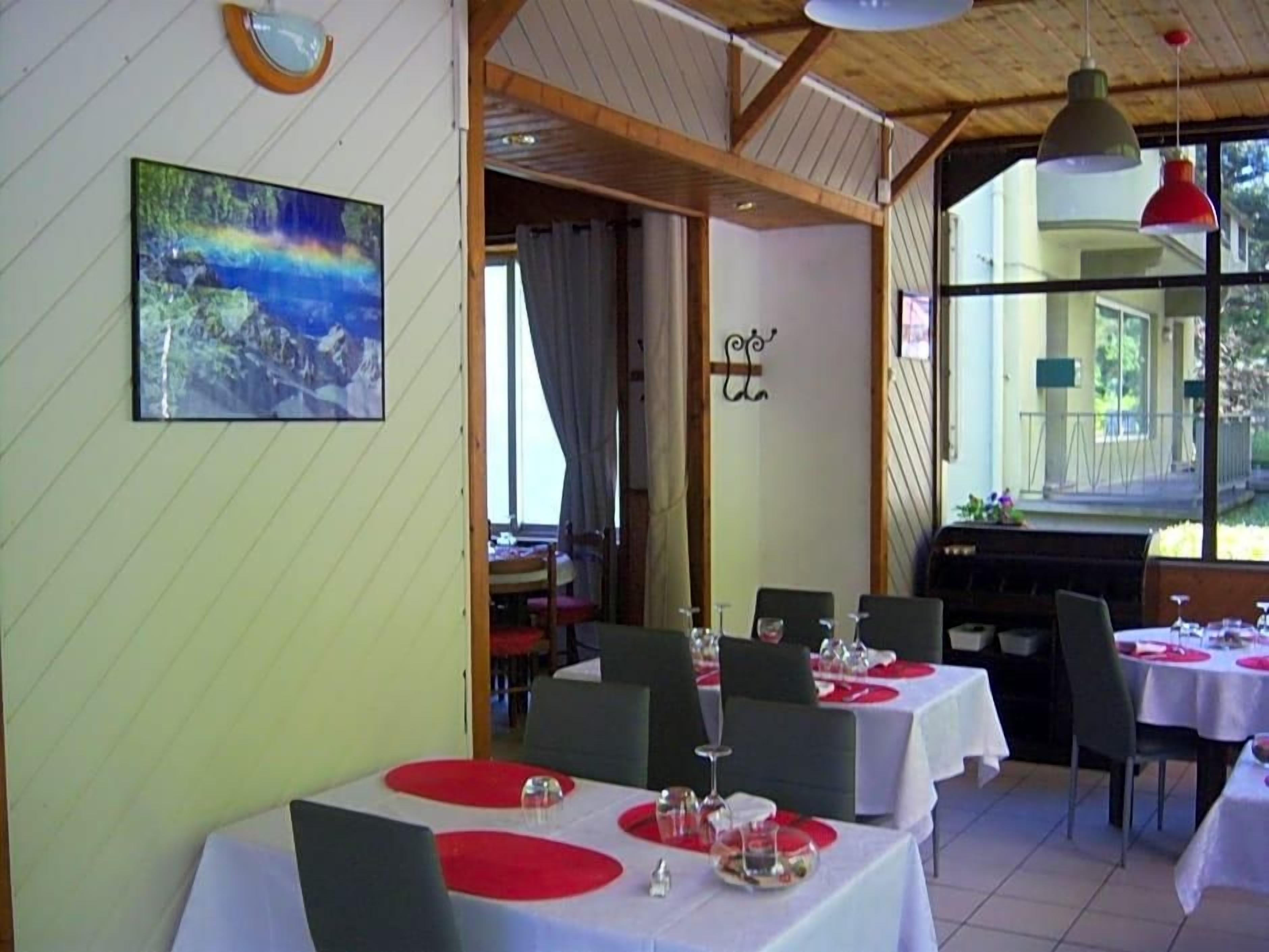 Interior de restaurante con mesas dispuestas para comer, un cuadro en la pared y vistas a través de la ventana.