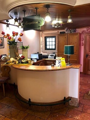 Et receptionområde med en buet disk, receptionsskilt, et skrivebord med computer, telefon og en vase med blomster.