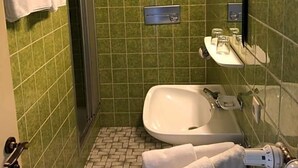 Een badkamer met groene tegels, een witte wastafel, een douche en een handdoekhouder.