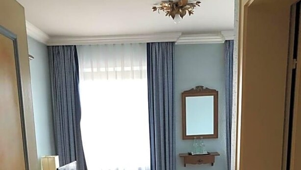 Een kamer met een houten vloer, een bureau met stoel, een kleine tafel, een spiegel en gordijnen.