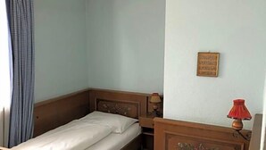 Een kamer met twee eenpersoonsbedden, een klein tafeltje, een lamp en een ingelijst beeld aan de muur.
