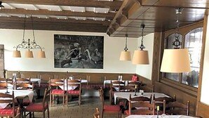 Een restaurant met houten balken, tafels met witte tafelkleden en rode stoelen met kussens.