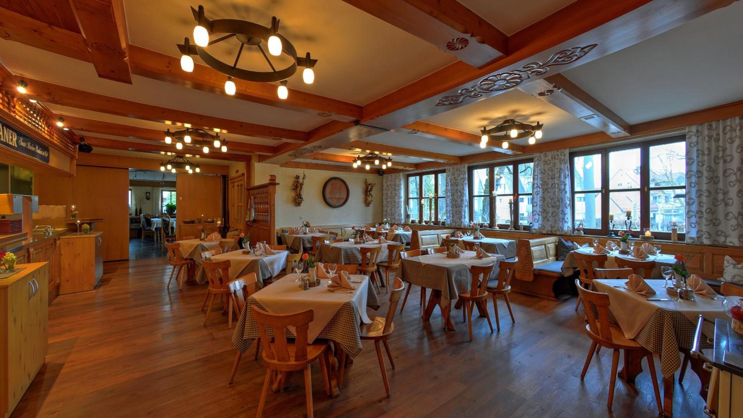 A restaurant with wooden interiors, multiple tables, and a view through large windows.