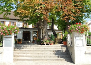 A building with a staircase leading to an entrance, surrounded by trees and potted plants. - Hotel Gasthof Grovu (Bergkirchen)