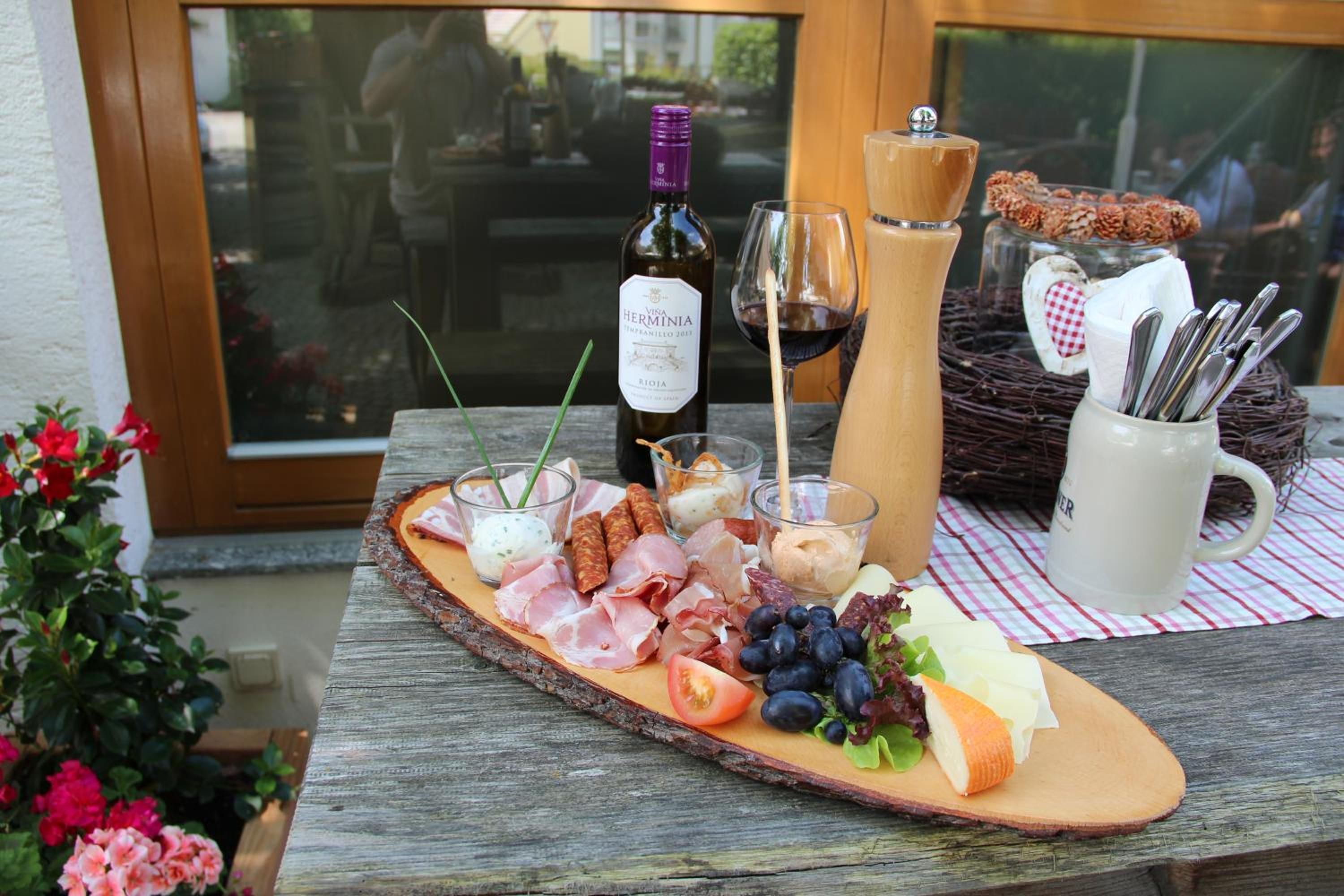 A wooden board with a variety of food items including meats, cheeses, and fruits, accompanied by a bottle of wine and glasses.