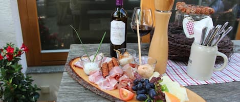 A wooden board with a variety of food items including meats, cheeses, and fruits, accompanied by a bottle of wine and glasses.