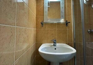 Un baño con un lavamanos blanco, cabina de ducha con paredes de vidrio y un espejo con adornos en espiral.