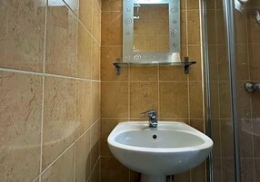 Un baño con un lavamanos blanco, cabina de ducha con paredes de vidrio y un espejo con adornos en espiral.