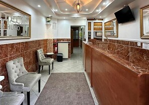 Un vestíbulo de hotel con paredes de mármol, una zona de estar, mostrador de recepción y un televisor montado en la pared.