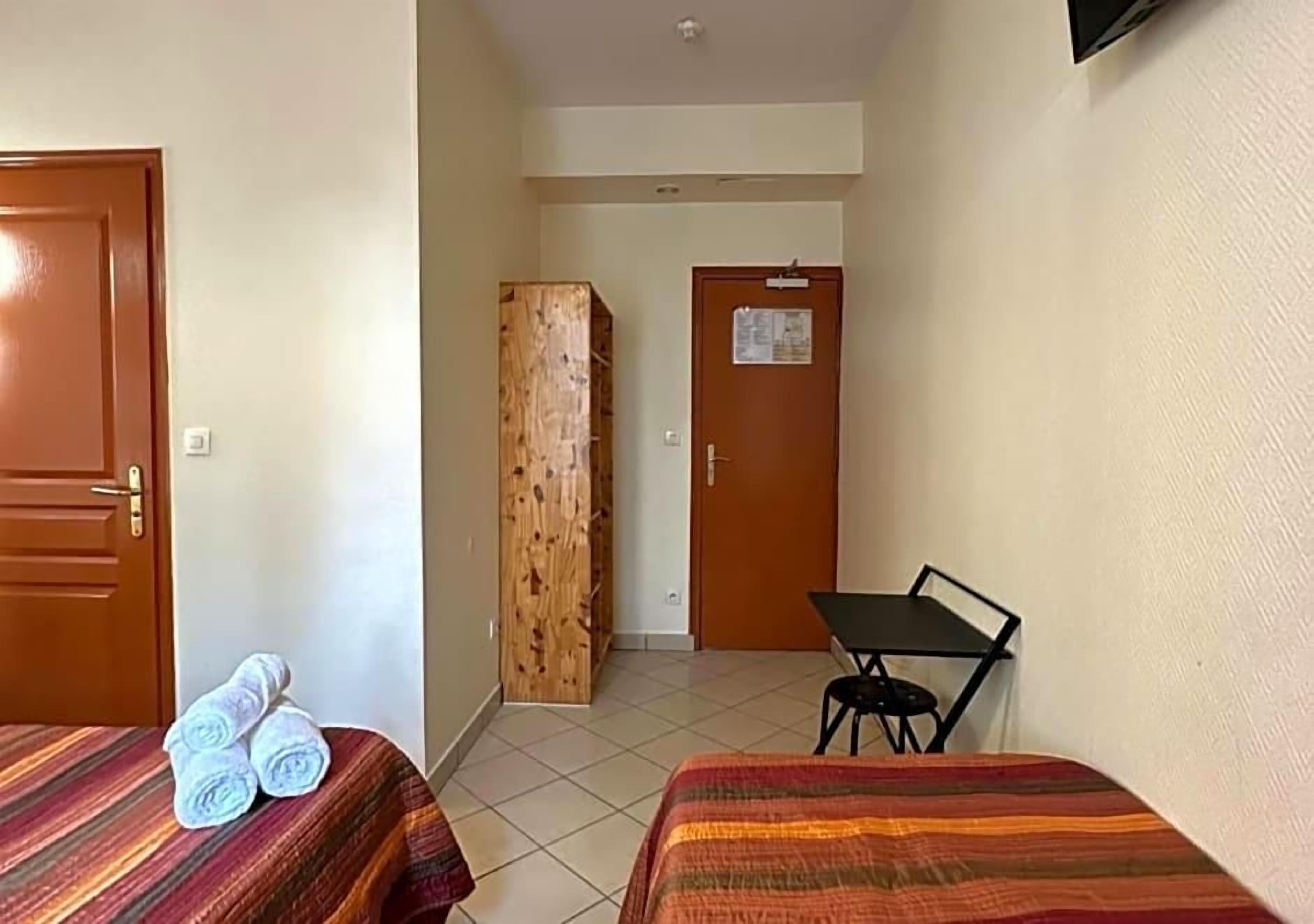 Habitación de hotel con dos camas, un armario de madera, una mesita y una puerta con un tablón de anuncios.