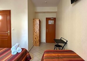 Habitación de hotel con dos camas, un armario de madera, una mesita y una puerta con un tablón de anuncios.