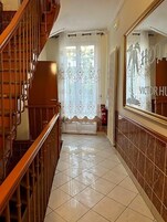 Un pasillo con una escalera de madera, un radiador y un espejo que refleja a una persona.
