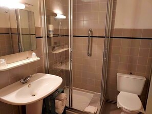 Un baño con ducha envuelta en vidrio, un lavamanos blanco y un inodoro.