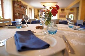 Una mesa de comedor dispuesta con platos, cubiertos y vasos, con una servilleta doblada y un jarrón con flores al fondo.
