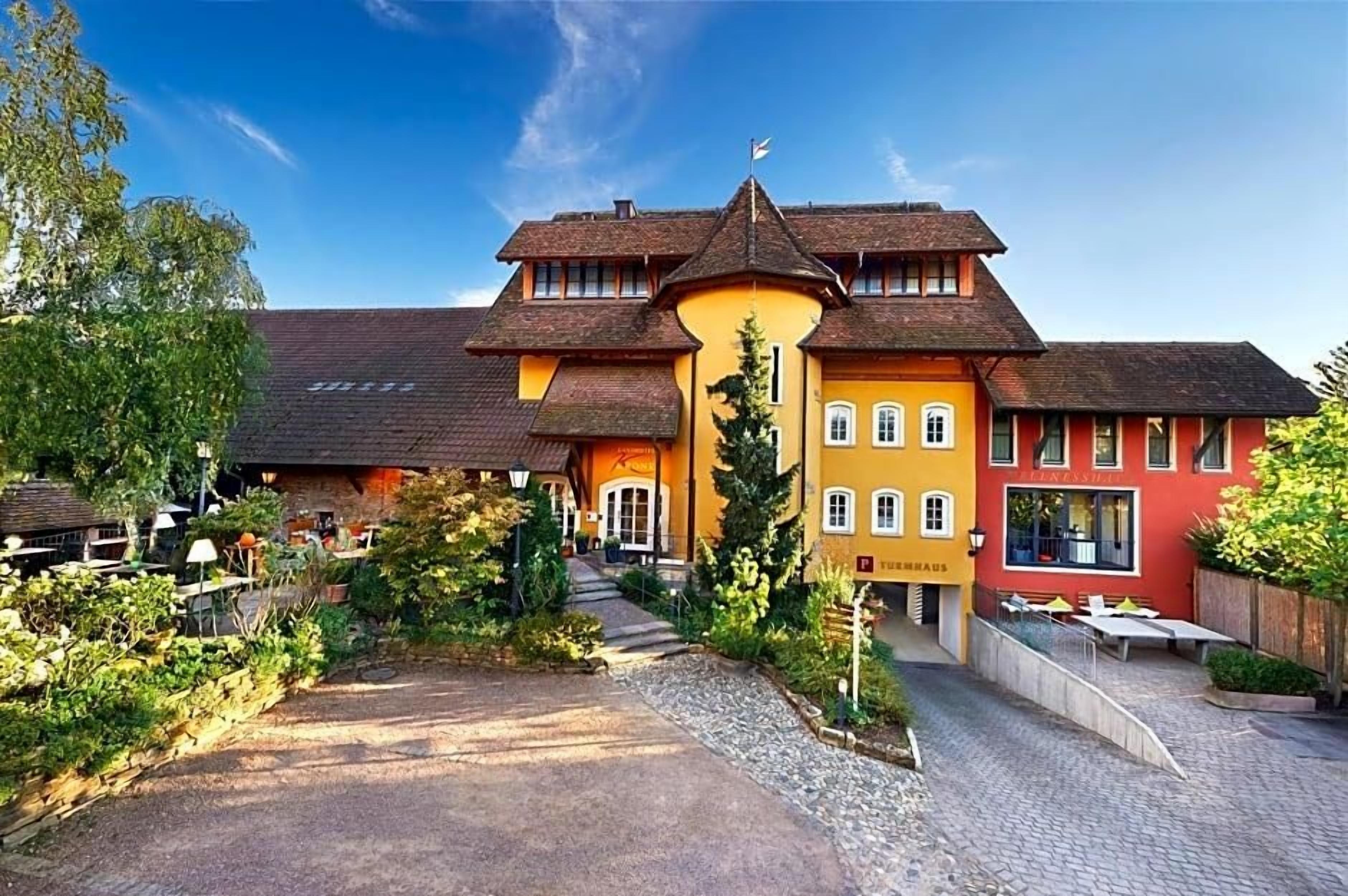 Ein traditionelles Gebäude mit einem zentralen Eingang, einer überdachten Außenbestuhlung und einer Flagge auf dem Dach.