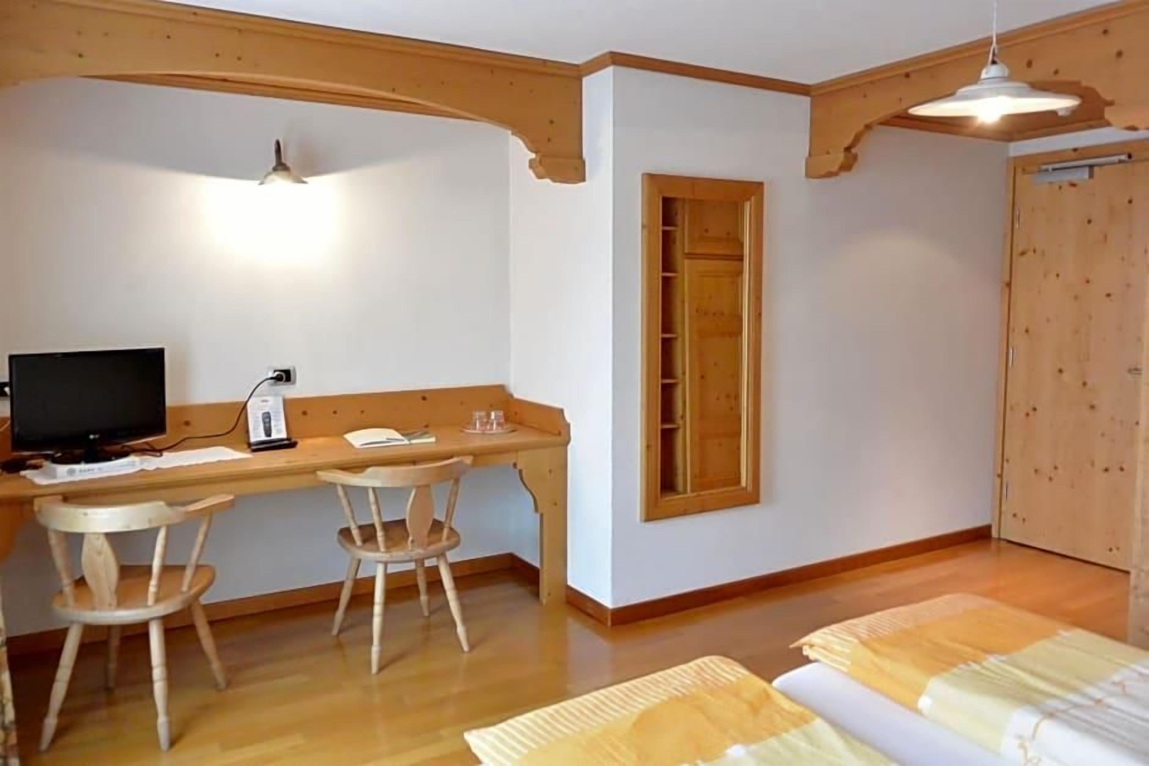 A room with a wooden desk, two chairs, a television, and a bed with a patterned bedspread.