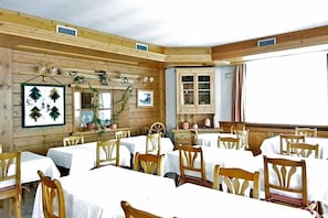 Zona pranzo con pareti in legno, tovaglie bianche e sedie di legno.