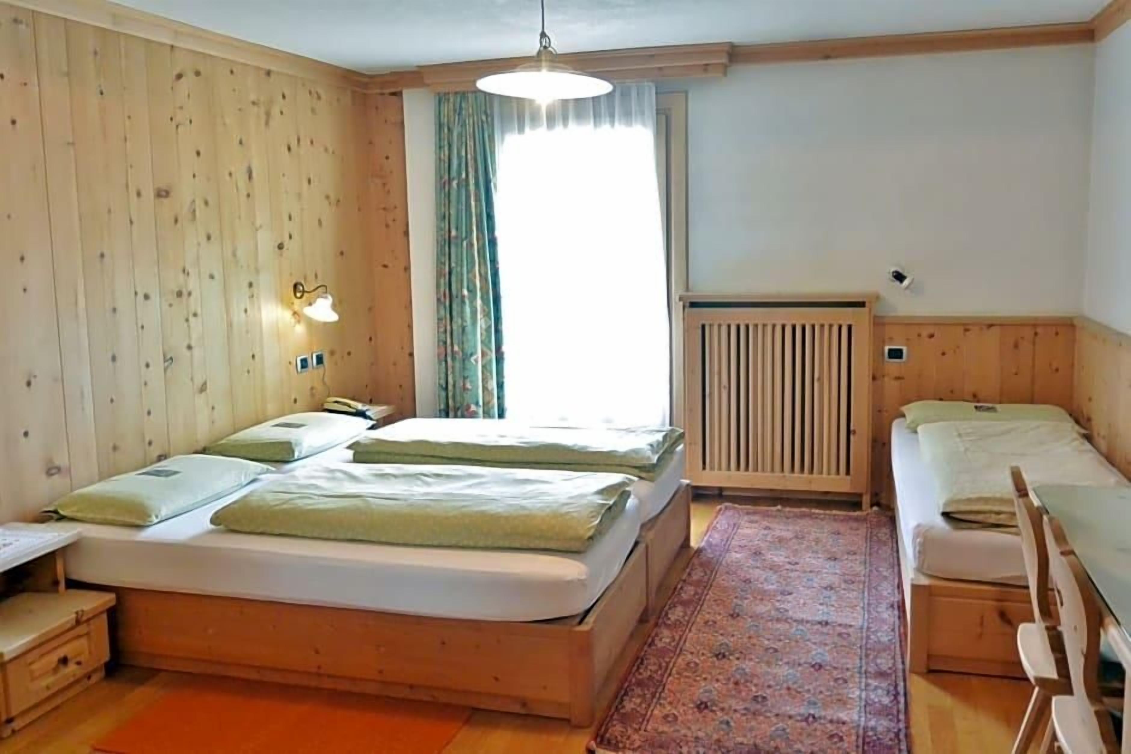 Une chambre avec un grand lit, un plus petit lit, un radiateur et une fenêtre avec des rideaux.