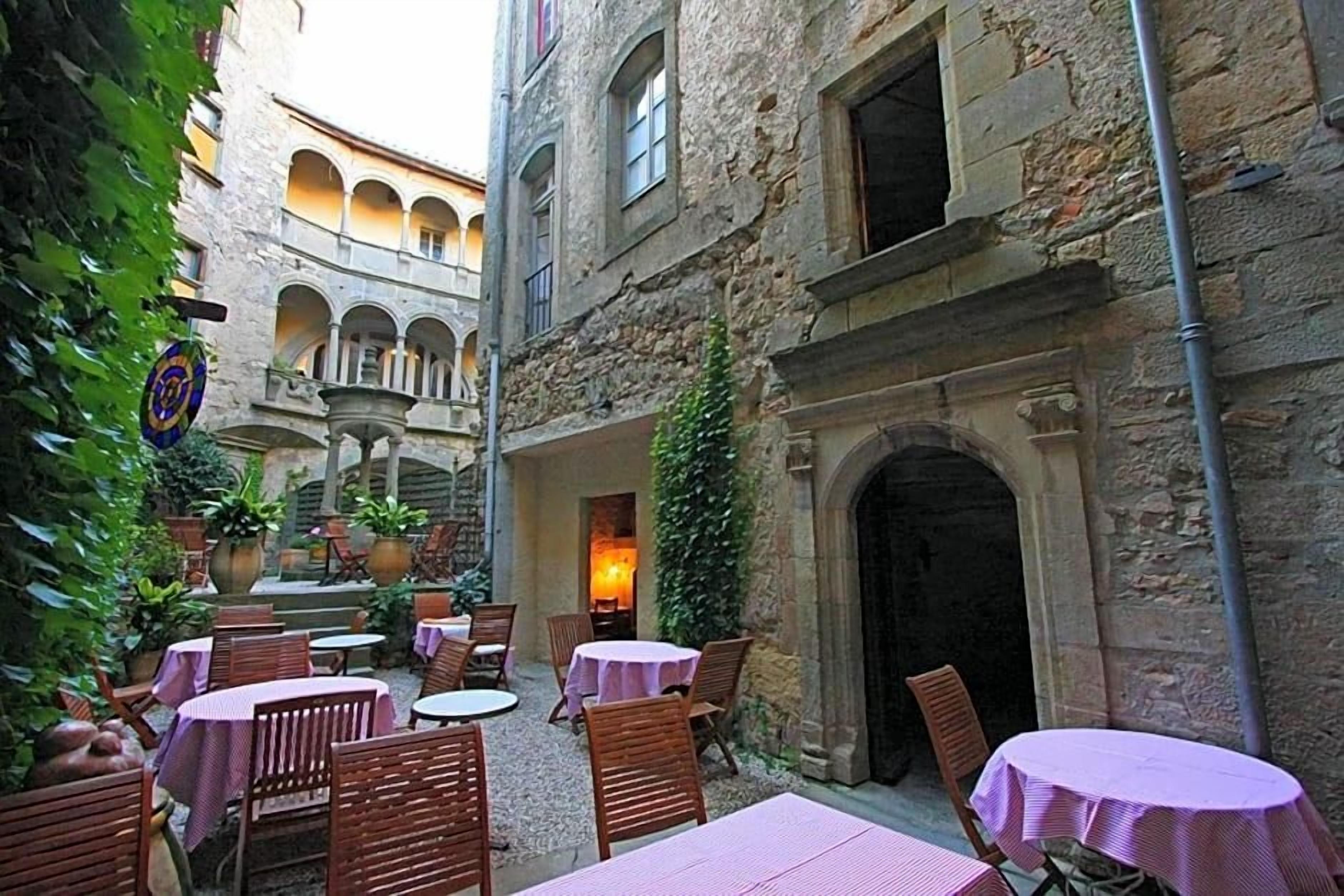 An outdoor courtyard with tables and chairs, stone buildings, and a fountain.
