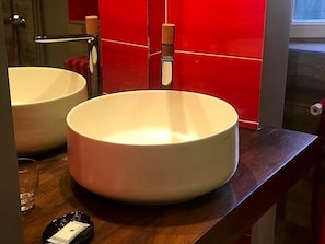 Un baño con dos lavamanos blancos y redondos, una encimera de madera y una pared con azulejos rojos.