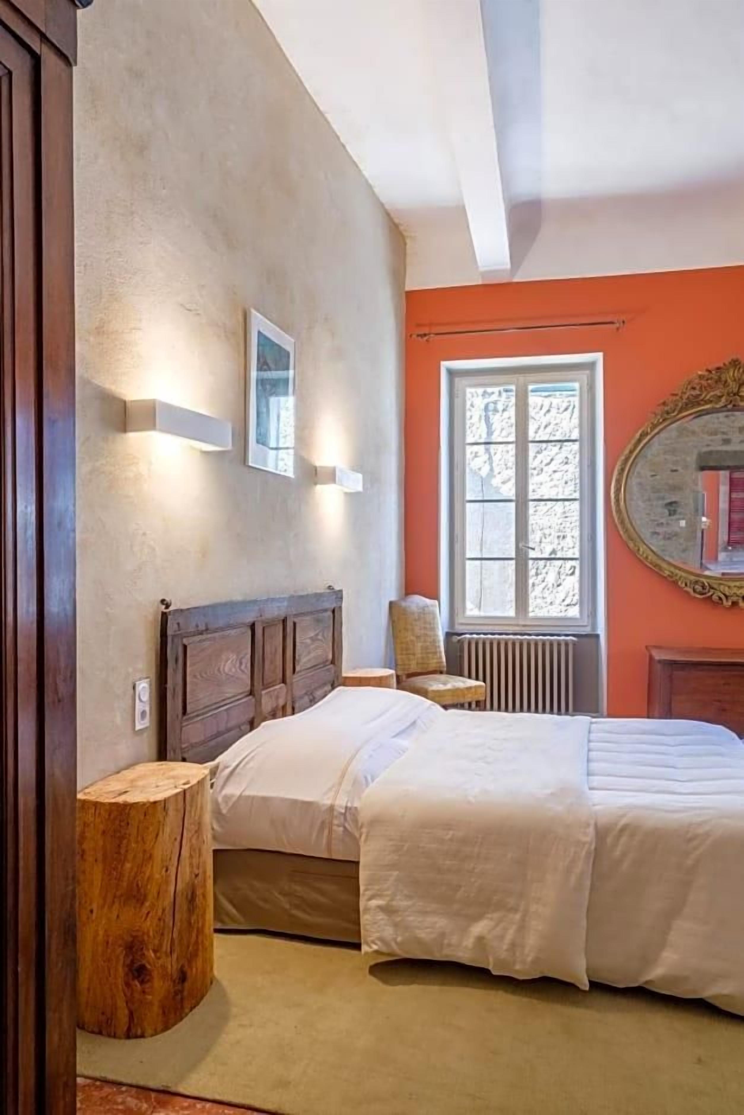 A bedroom with a large bed, a chair, a wooden nightstand, and a window with a view.