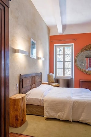 Un dormitorio con una cama grande, una silla, una mesita de noche de madera y una ventana con vistas.