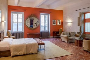 Une chambre à coucher avec un lit, deux chaises, un miroir rond et une fenêtre.