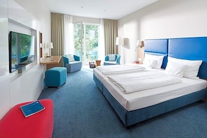 Habitación de hotel con una cama grande, un escritorio con silla, televisión y balcón con vistas.