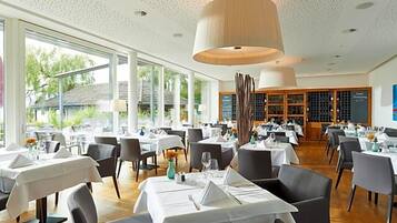 Restaurante com várias mesas, toalhas brancas e um grande lustre pendente.