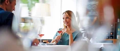 Un comedor con una mesa preparada para dos personas, una copa de vino tinto y una vela sobre la mesa.
