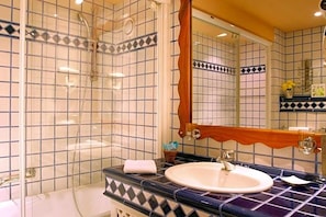 Um banheiro com chuveiro em azulejo, pia com espelho e detalhes decorativos na parede.